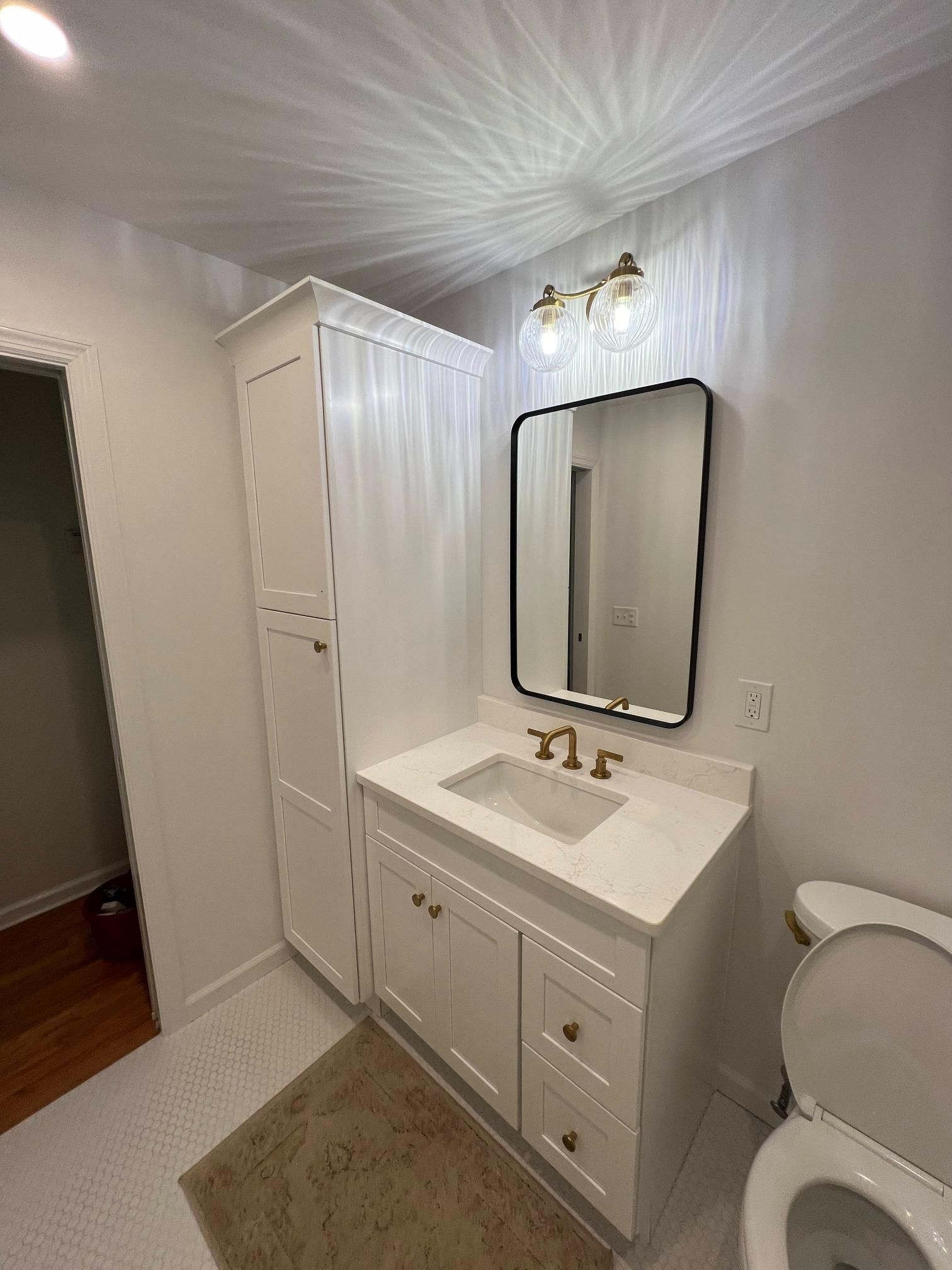 Small white bathroom with vanity, mirror, cabinet, shower curtain, and toilet visible.