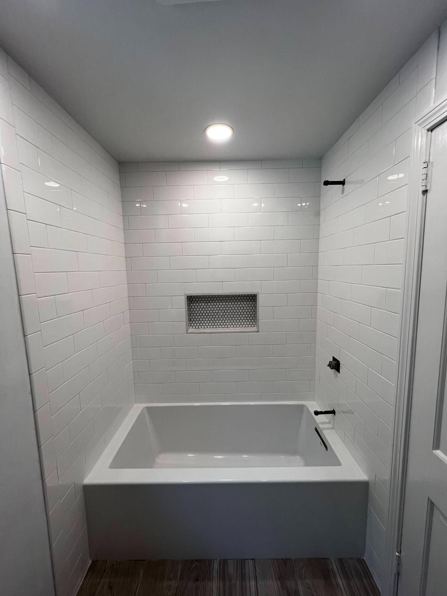 White tiled bathroom with a built-in rectangular soaking tub and small recessed wall niche.