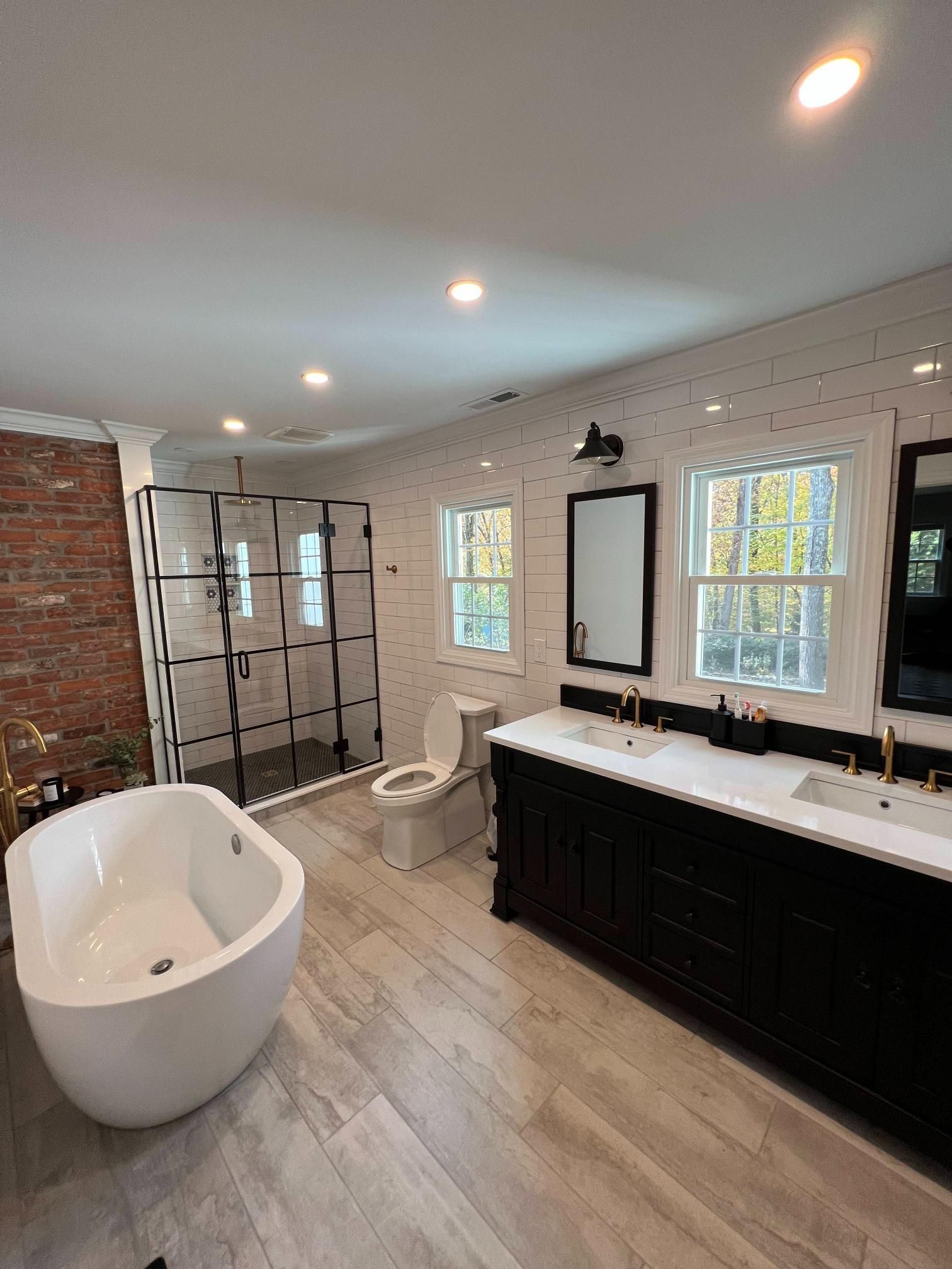 Modern bathroom with freestanding tub, black vanity, double windows, and walk-in shower with tiled walls