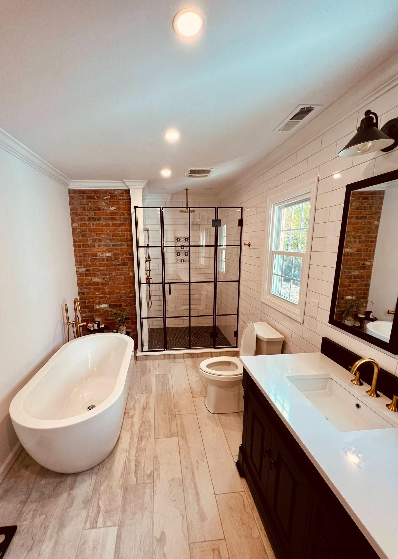 Bright modern bathroom with freestanding tub, walk-in shower, vanity, and brick accent wall