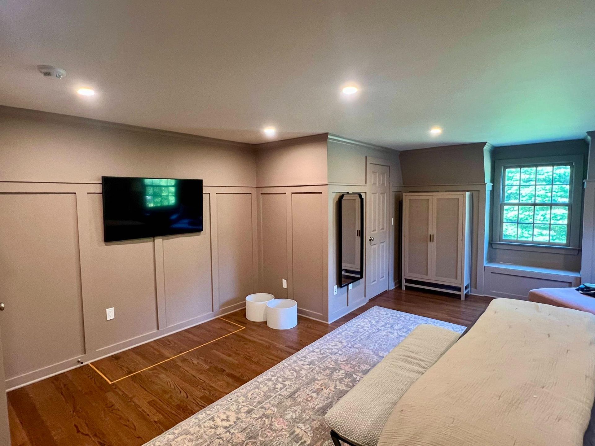 Modern bedroom with built-in cabinets, wall-mounted TV, mirror, window, and bed with gray bedding.