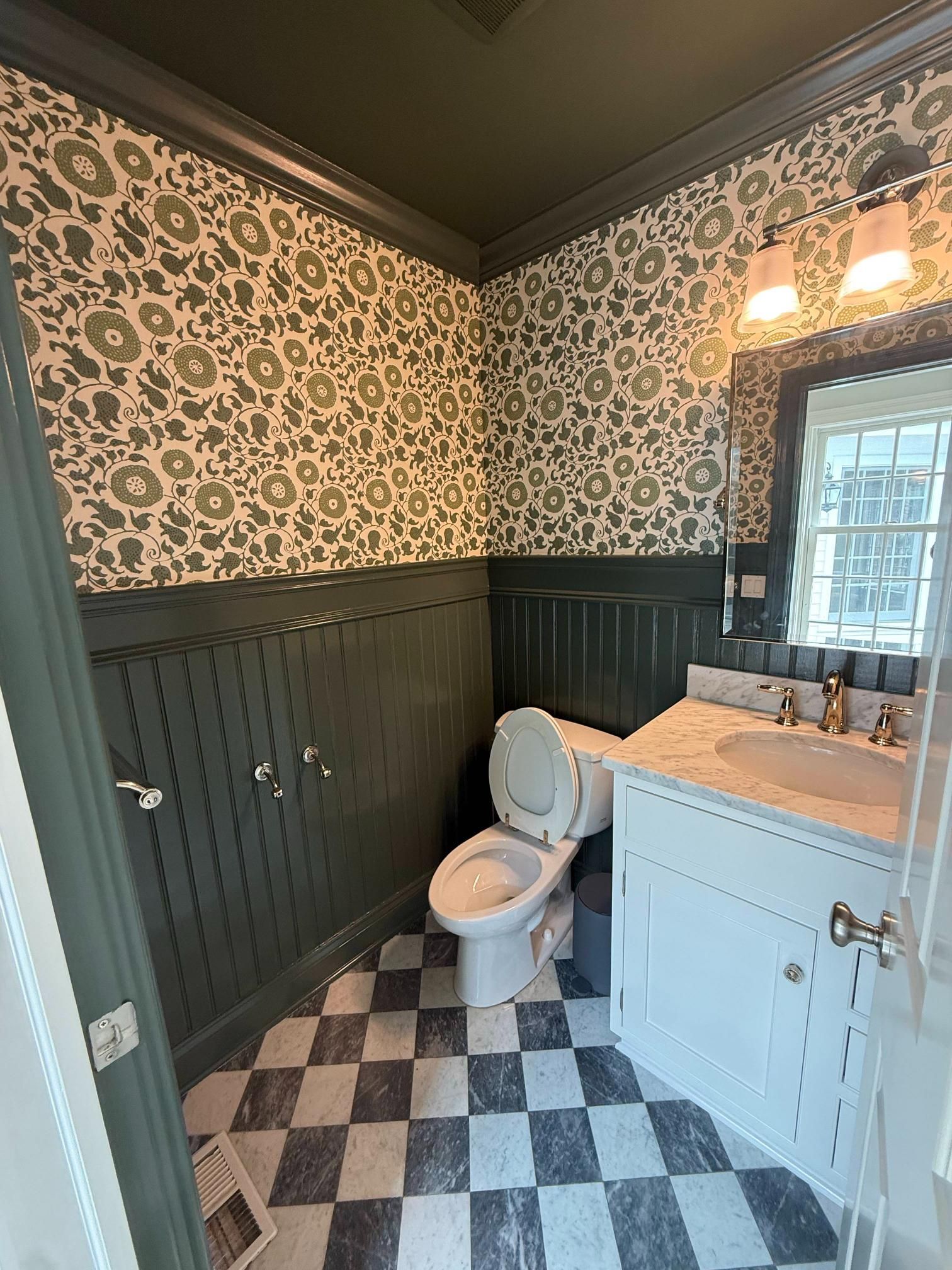 Small bathroom with patterned wallpaper, black-and-white checkered floor, toilet, and vanity sink.