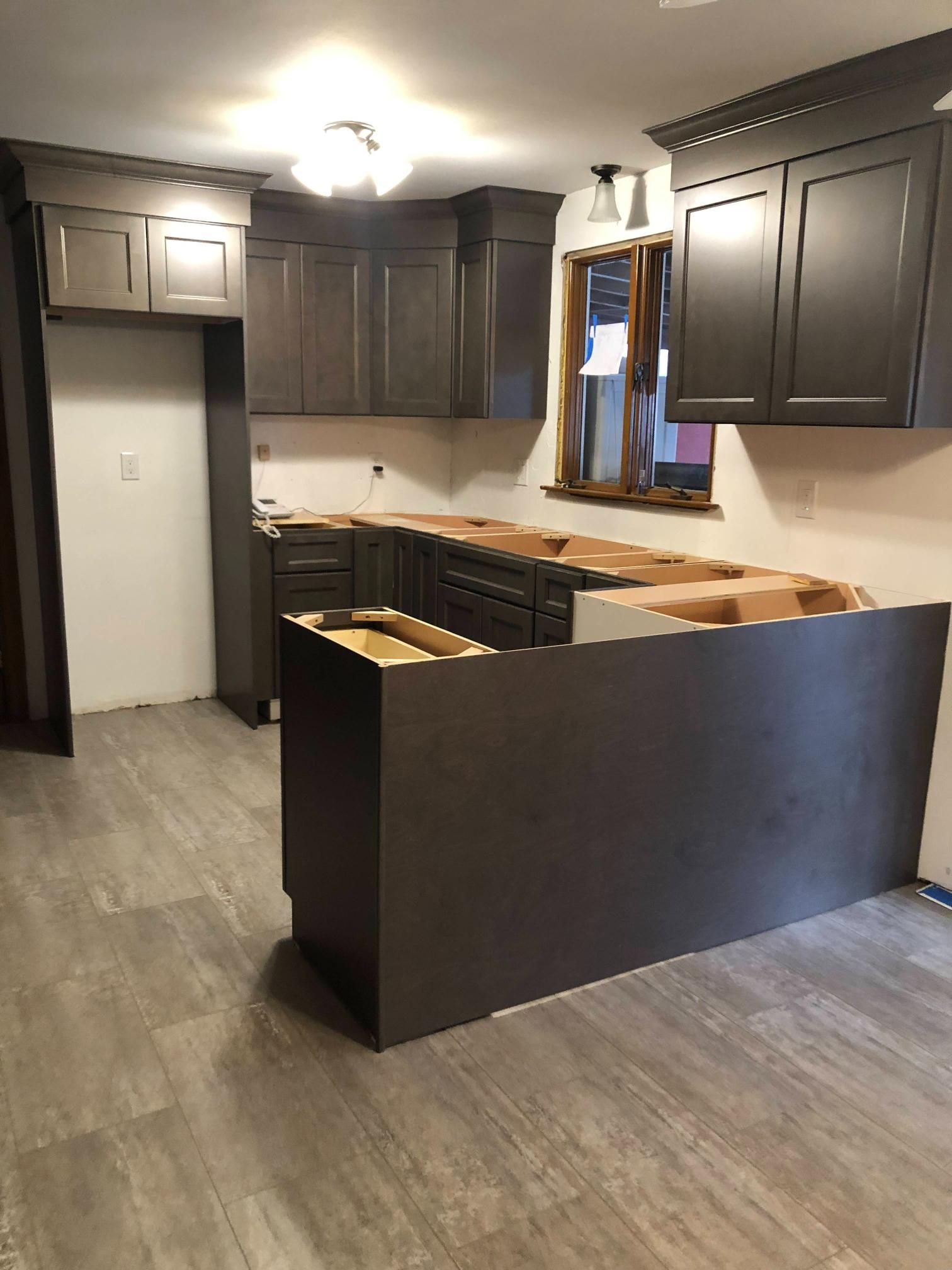 Unfinished kitchen with dark cabinets, gray flooring, and a partially installed island countertop.