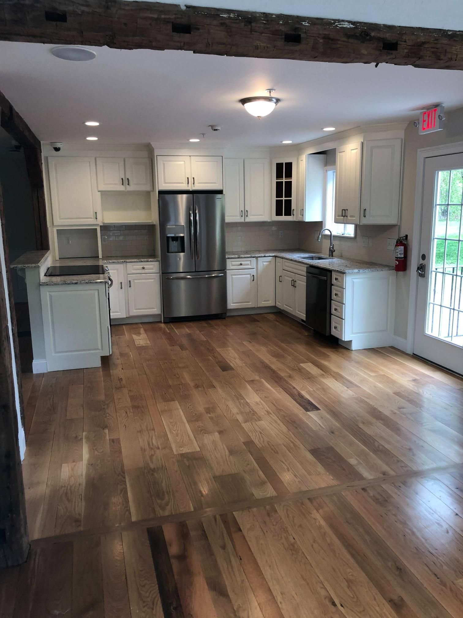 Bright kitchen with white cabinets, stainless fridge, wood floors, and a sliding glass door.
