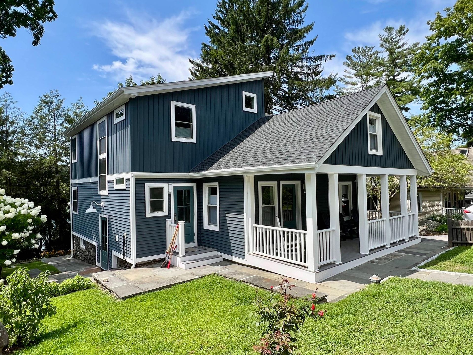 Blue two-story house with white trim, front porch, and green lawn under a sunny sky