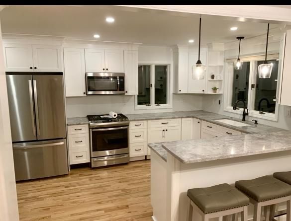 Bright white modern kitchen with stainless steel appliances, marble counters, island stools, and hardwood floors