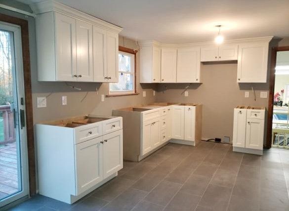 Empty modern kitchen with white cabinets, gray tile floor, and a sliding glass door to the left