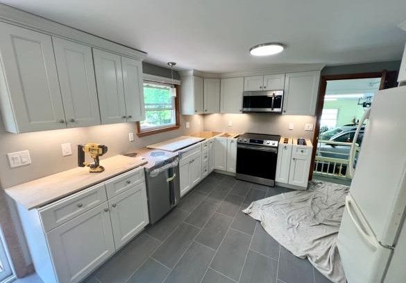 Bright modern kitchen with white cabinets, gray tile floor, and stainless steel appliances
