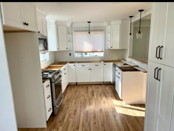 Bright white kitchen with wood countertops, black hardware, and a wood floor, lit by daylight.