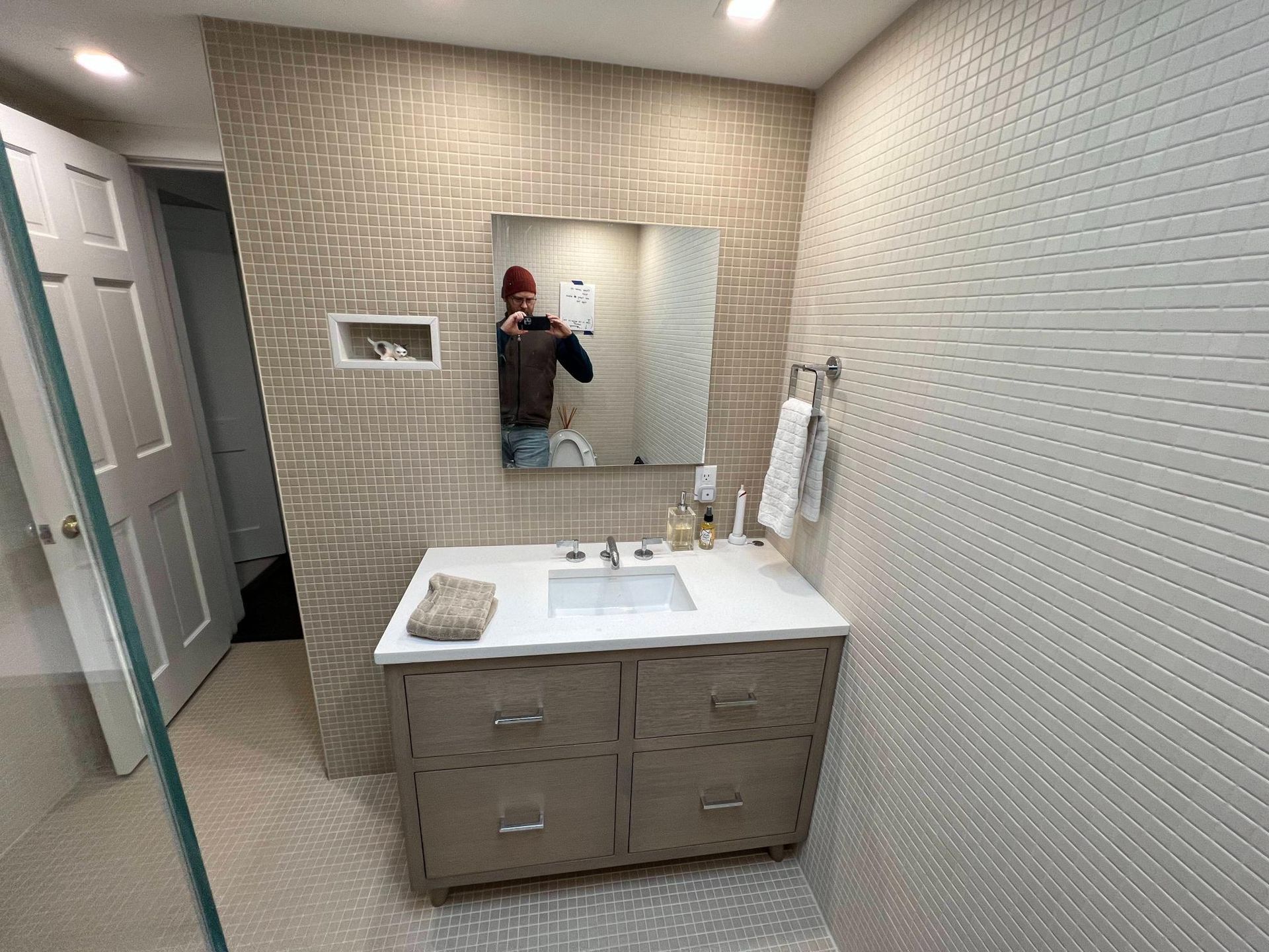 Modern bathroom vanity with mirror, beige tiled walls, and a person taking the photo in the mirror.