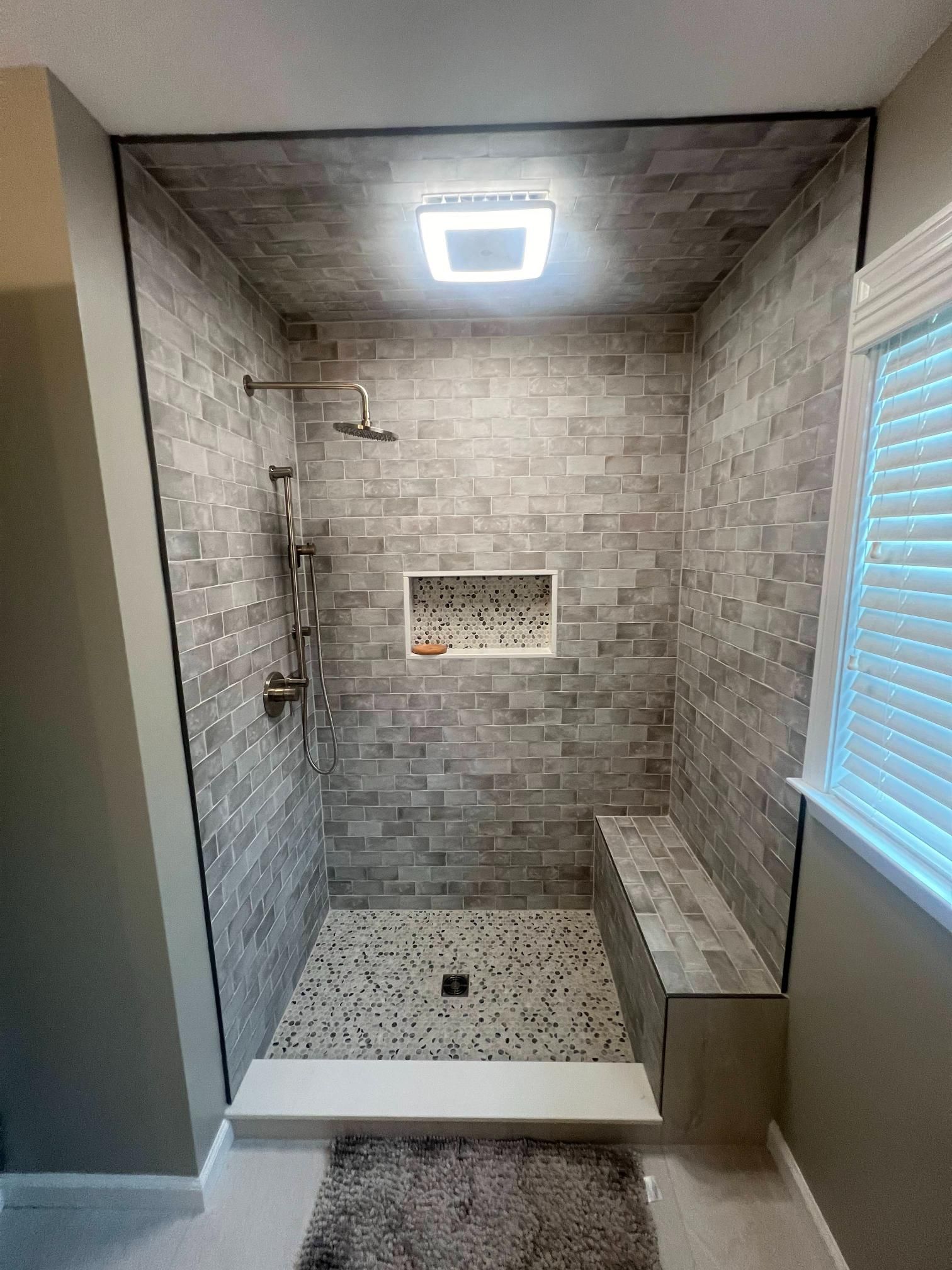 Modern tiled walk-in shower with a bench, rainfall head, niche, and window blinds