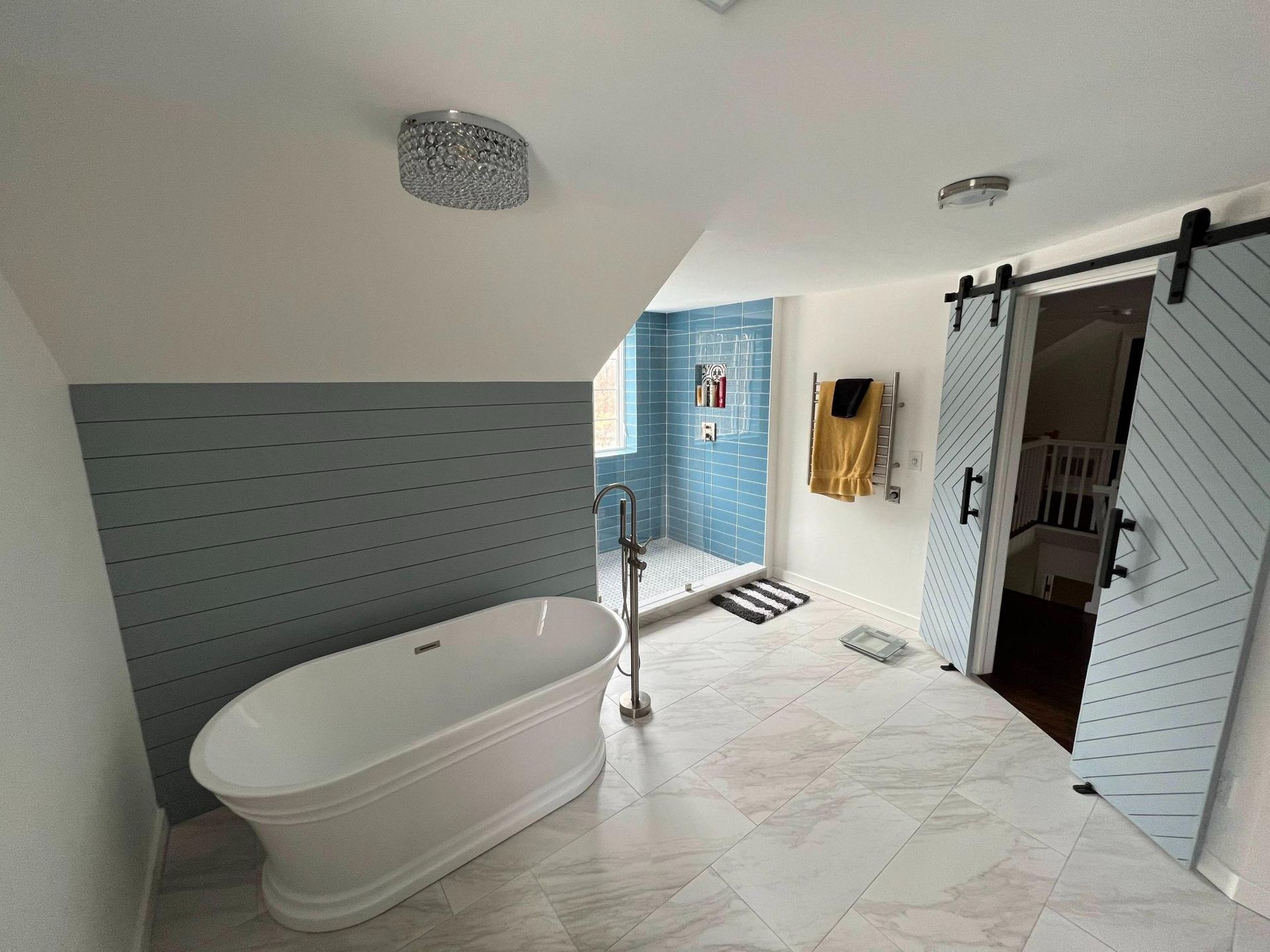 Modern bathroom with freestanding tub, walk-in shower, and white tile floor under sloped ceiling