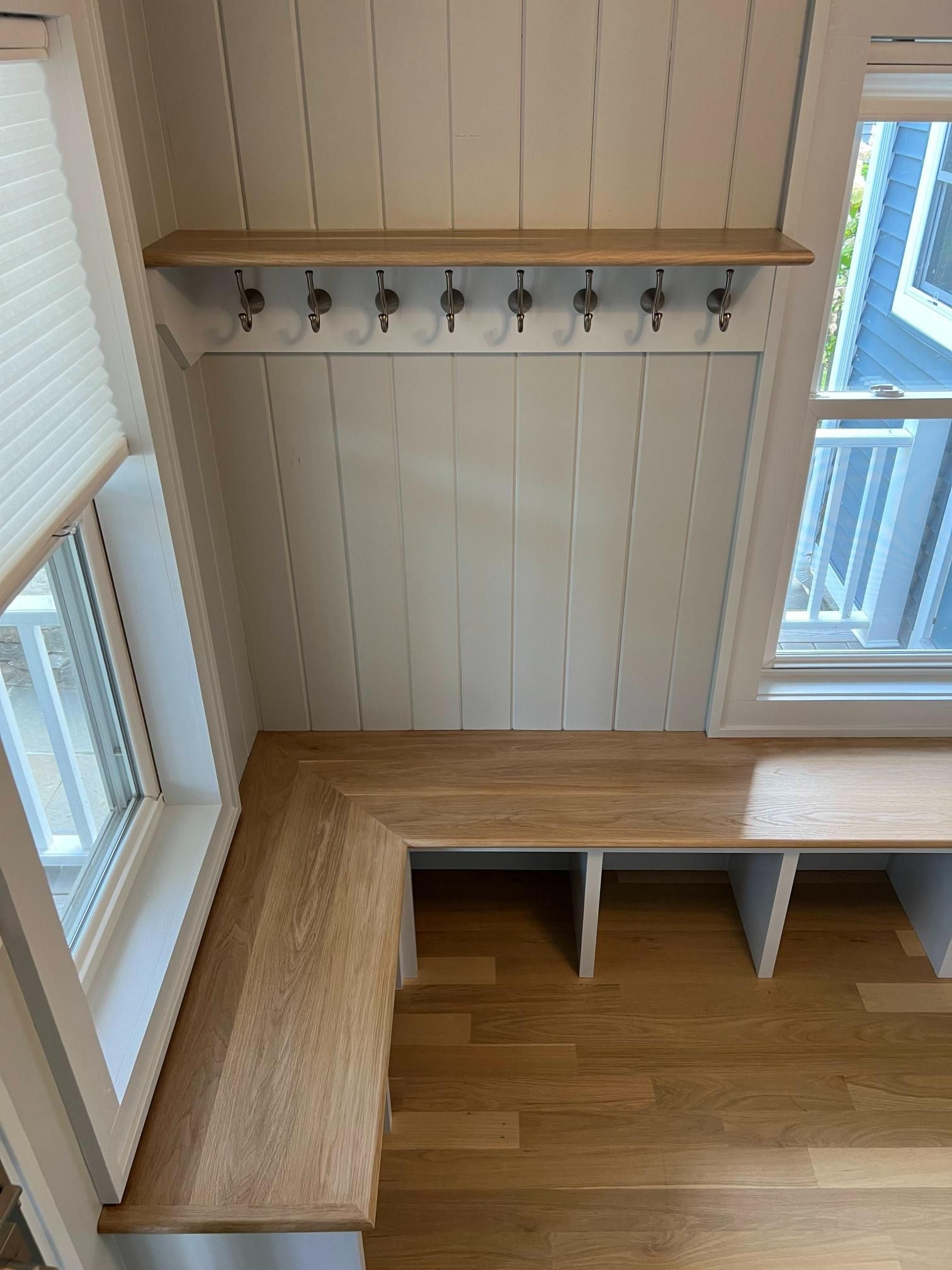 Built-in wooden bench under wall hooks beside windows in a bright entryway