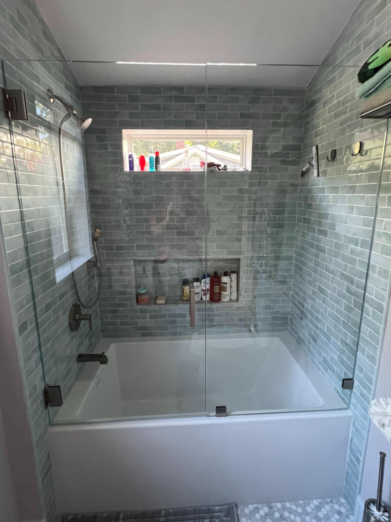 Modern bathroom with a white bathtub, gray tiled walls, and a small frosted window above the tub
