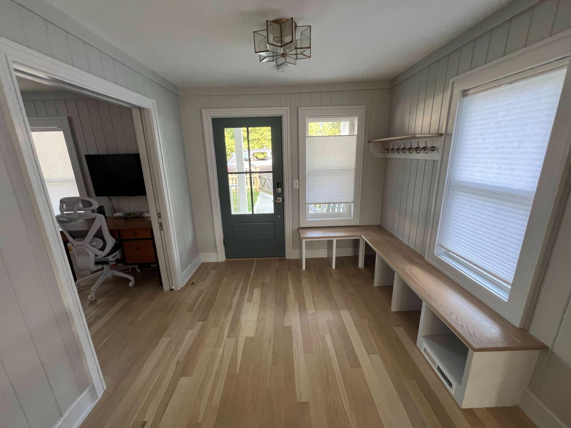 Bright entryway with light wood floors, green front door, bench seating, and windows with blinds