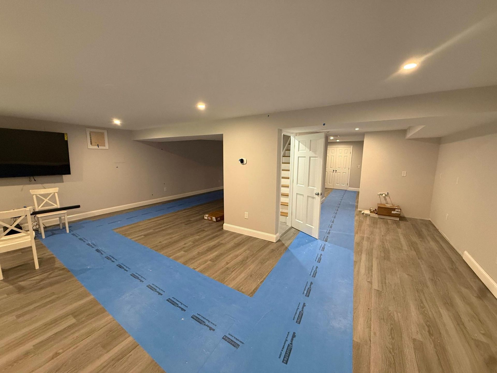 Empty living room with blue painter’s tape marking areas on the floor, white walls, and wood flooring.