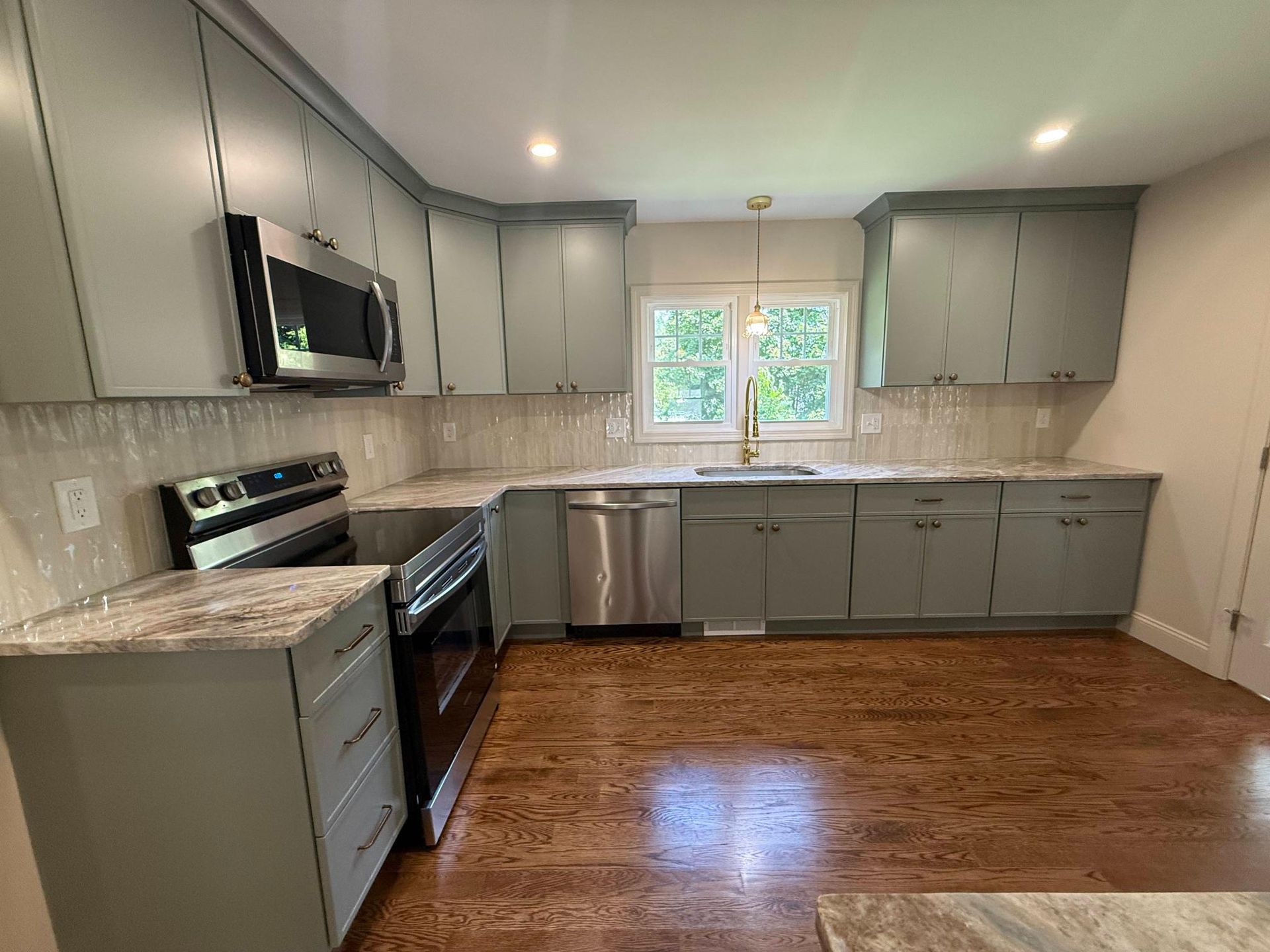 Modern kitchen with gray cabinets, stainless steel appliances, and a window over the sink, with wood floors.