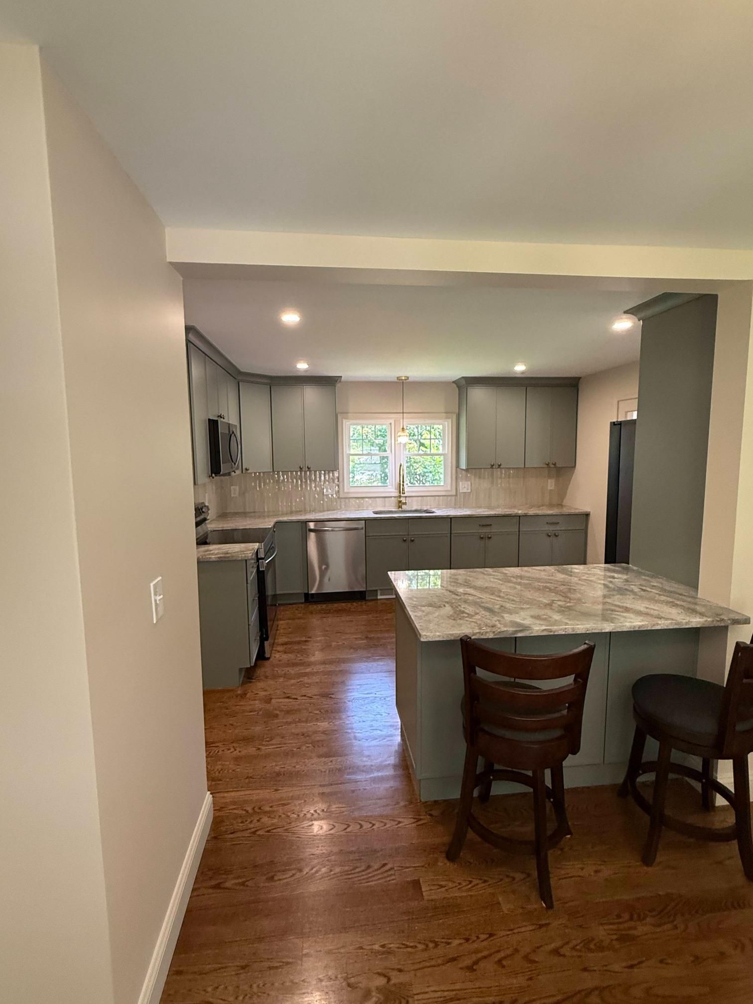 Modern kitchen with gray cabinets, wood floors, and a marble island with two chairs.