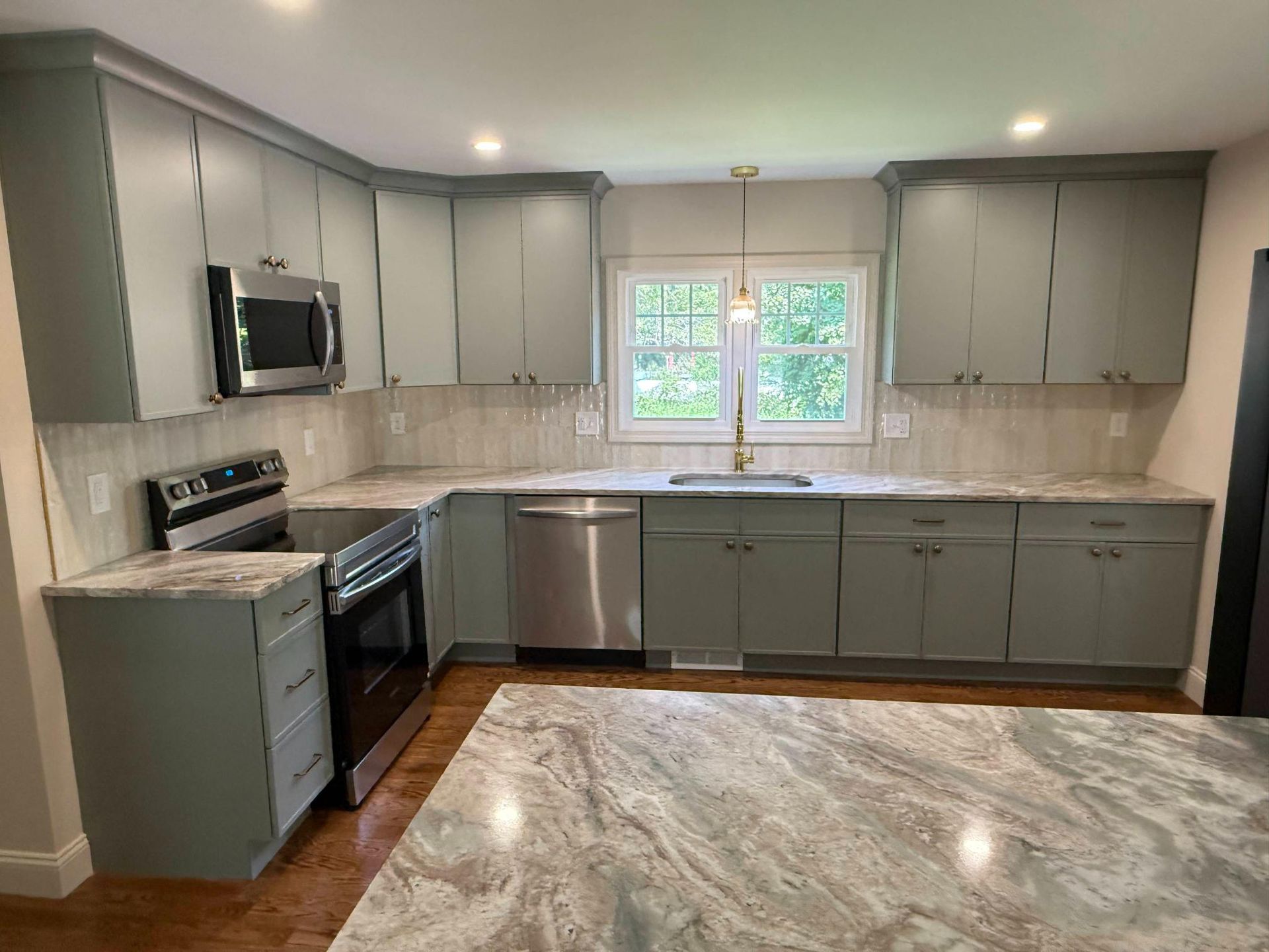Modern kitchen with gray cabinets, stainless appliances, and a window over the sink with marble-look flooring.