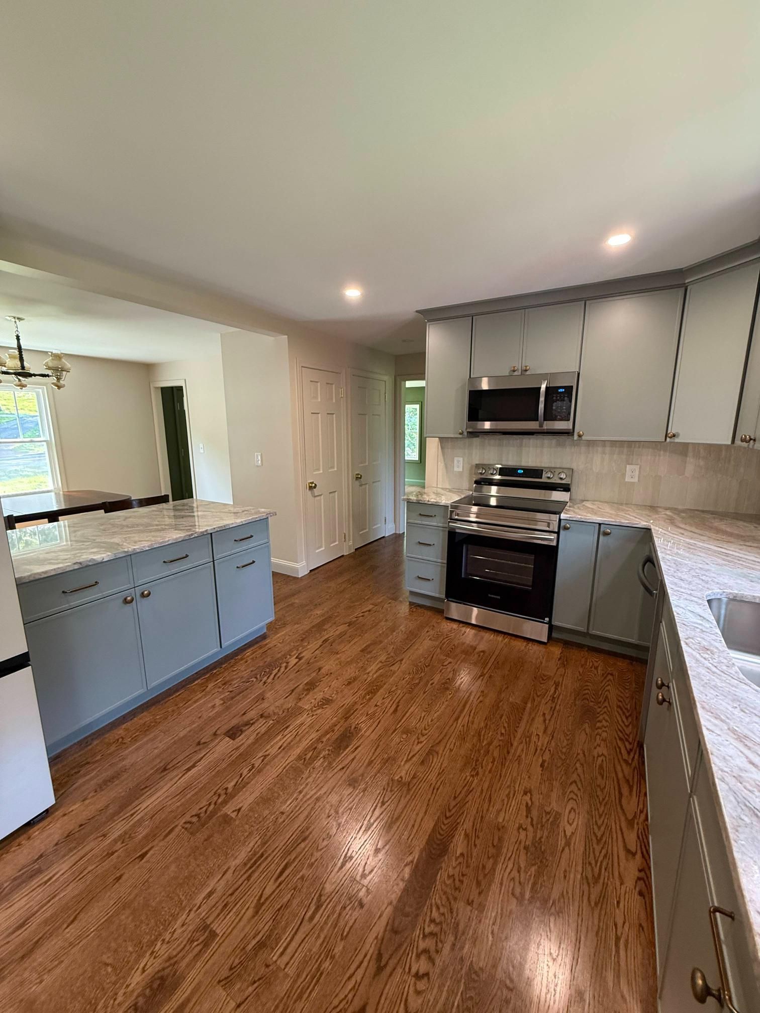 Bright kitchen with white cabinets, stainless stove, blue island cabinets, and wood floors
