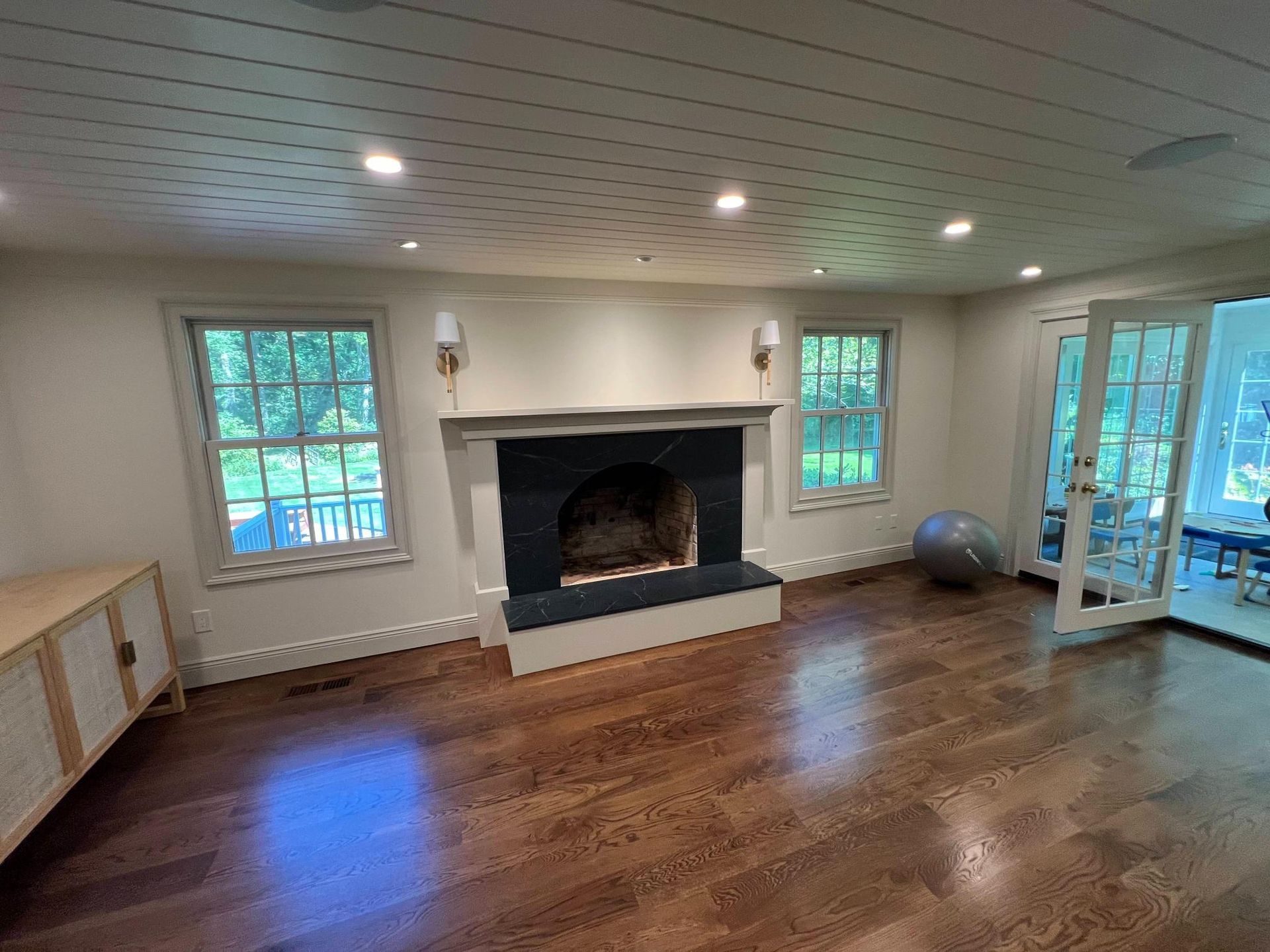Living room with hardwood floors, white fireplace, windows, and a glass door to the outside.