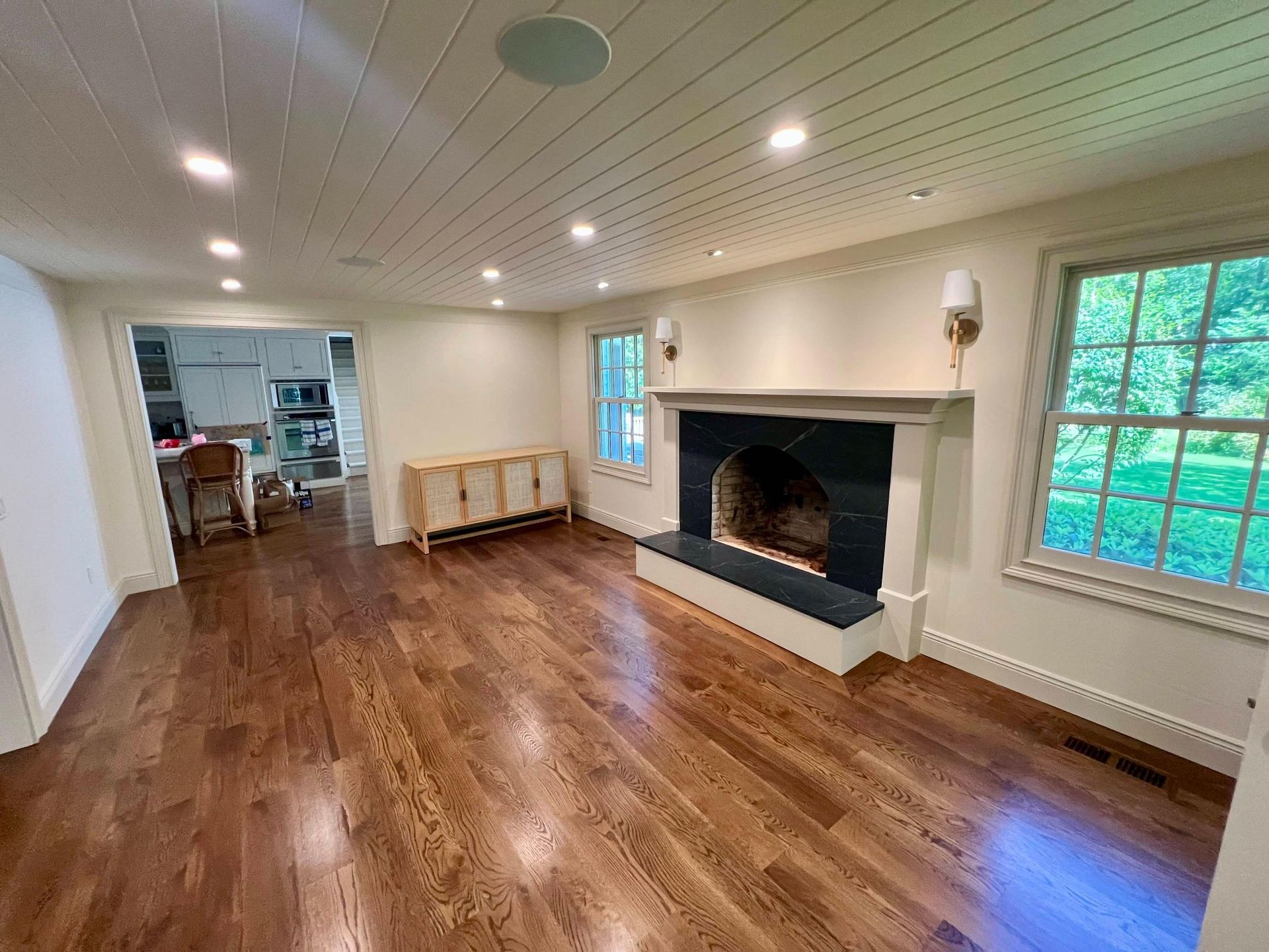 Empty living room with wood floors, white ceiling, and a large black fireplace mantle