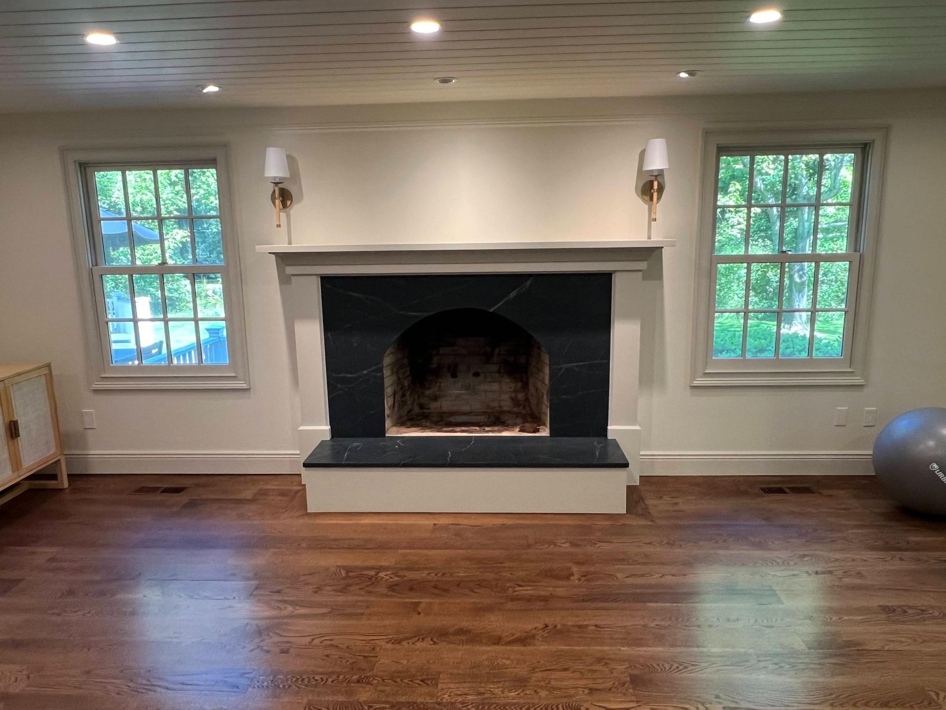 Living room with a large fireplace, two windows, hardwood floors, and a ceiling light.