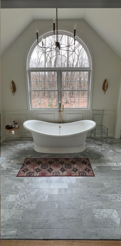 Bright white freestanding bathtub beneath a large arched window in a light gray bathroom.