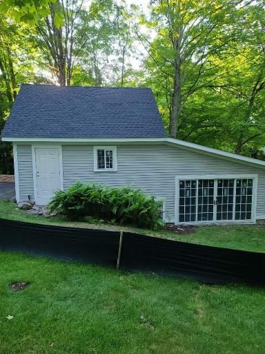 Small gray house with dark roof and large windows, surrounded by trees and grass behind a black fence