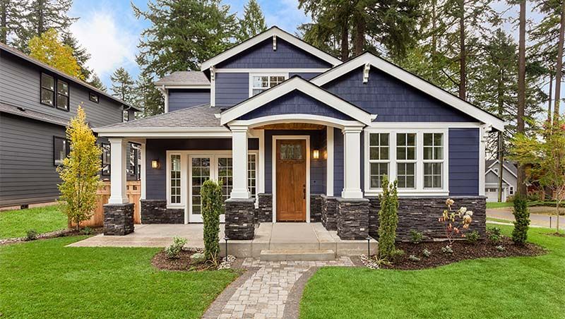 Modern blue-gray house with white trim, stone accents, front porch, and a lush green lawn
