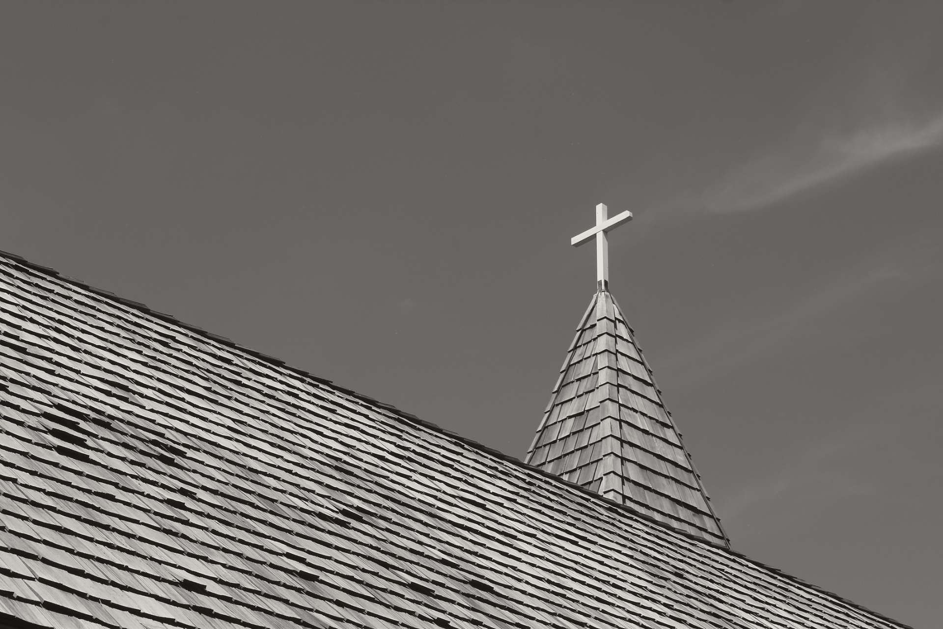 A black and white photo of a church steeple with a cross on top.