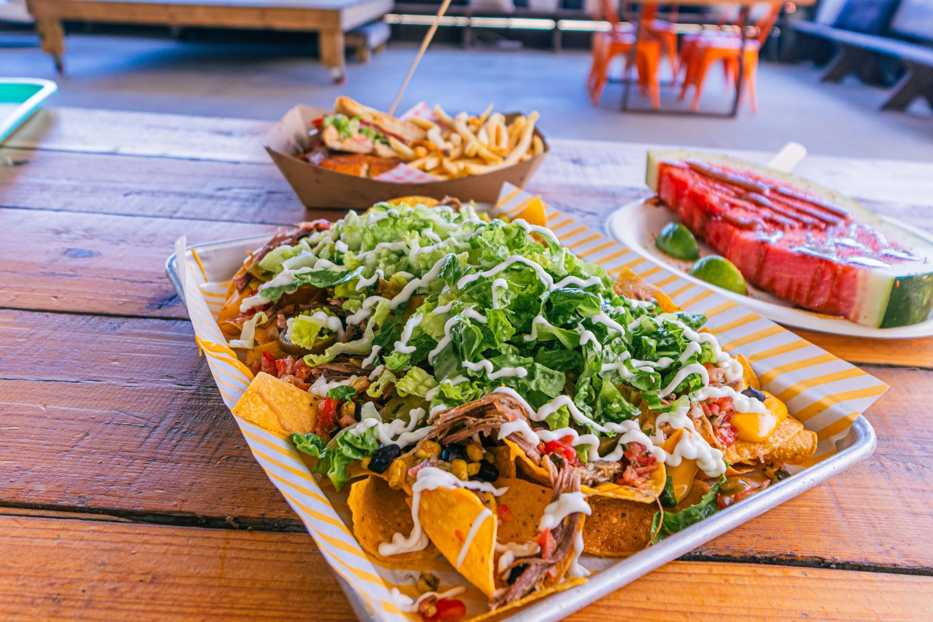 A tray of nachos and watermelon on a wooden table.