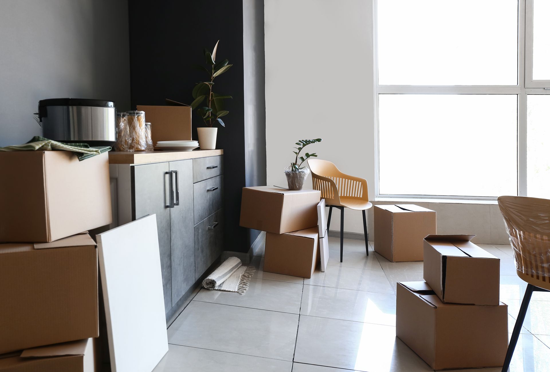 Moving boxes in a bright room with cabinets and a large window, suggesting a recent move.