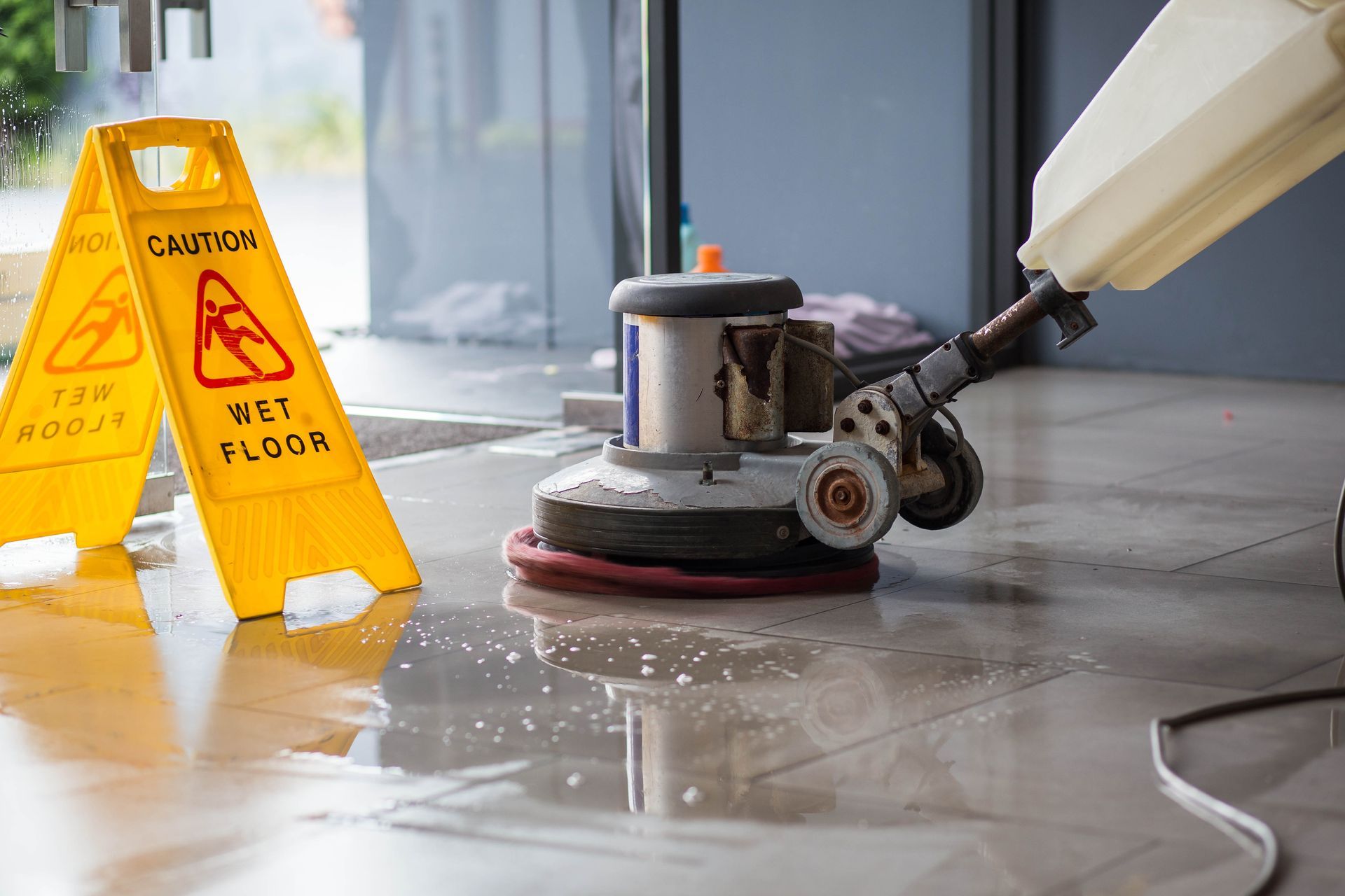 Floor cleaner polishing a wet surface beside yellow caution signs