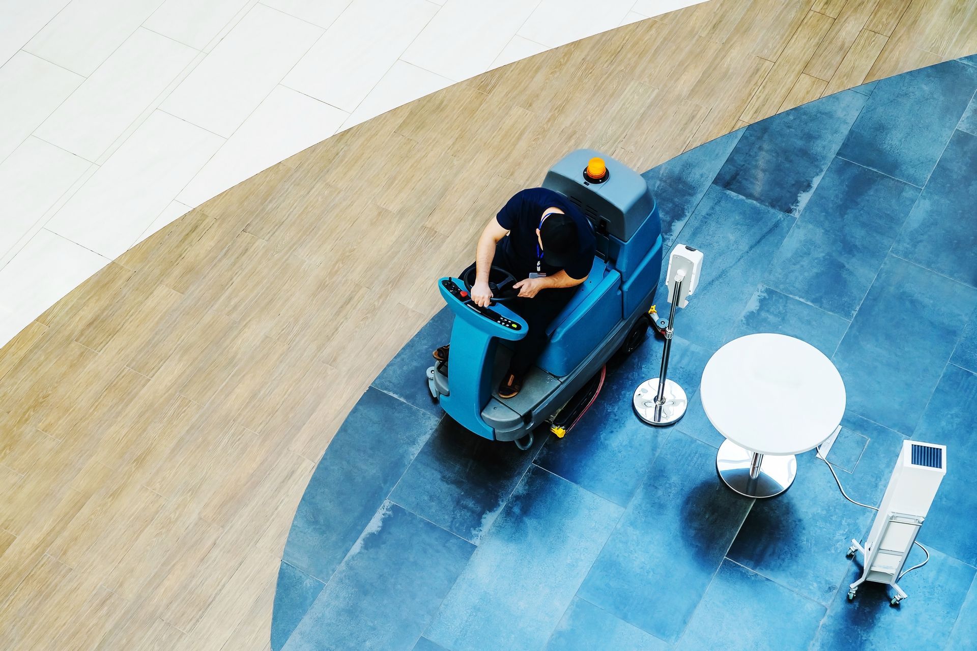 Person riding a blue mobility scooter in a spacious indoor area with a small white table nearby