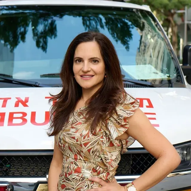 Woman in patterned dress smiles, stands in front of an ambulance.