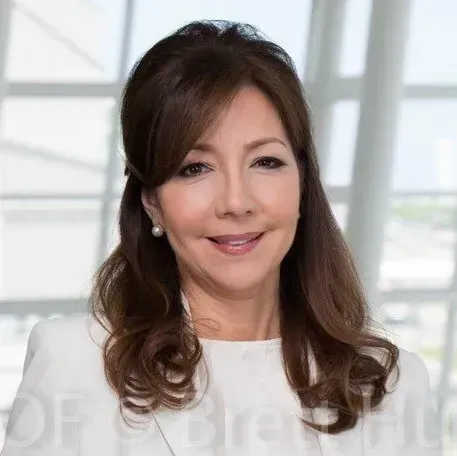 Woman in white blazer smiles, standing in a bright office space.
