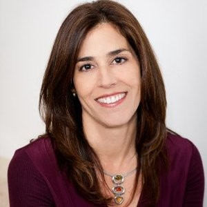 Woman with long brown hair, smiling, wearing a burgundy top and silver necklace.