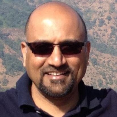Man with sunglasses, short beard, smiling; blurred mountain background.