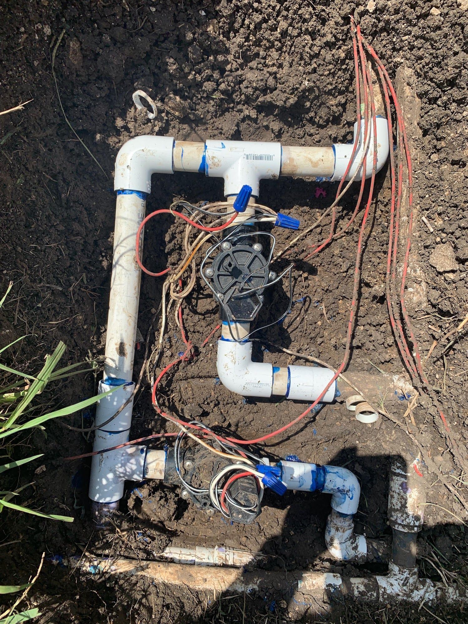 Irrigation system components: PVC pipes, valves, wiring, buried in soil.