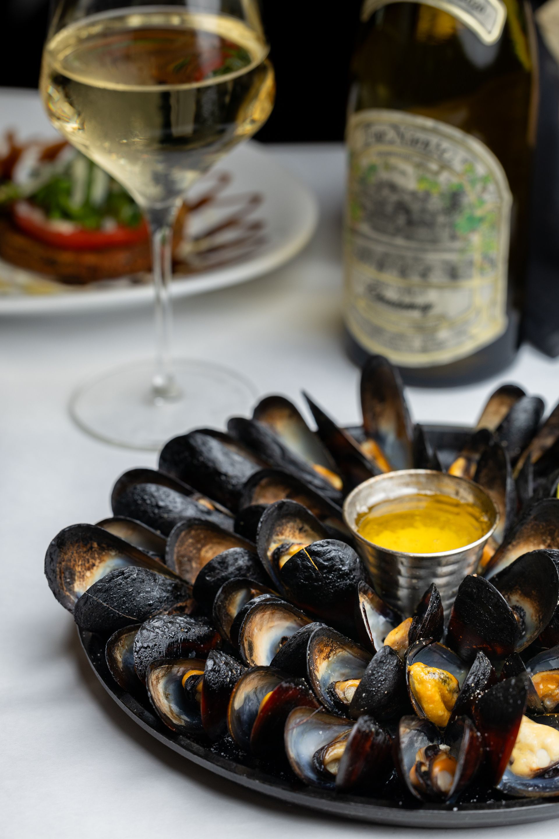 A plate of mussels and a glass of wine on a table.