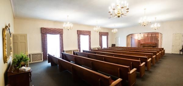 Empty church sanctuary with wooden pews, chandeliers, and windows along the side walls