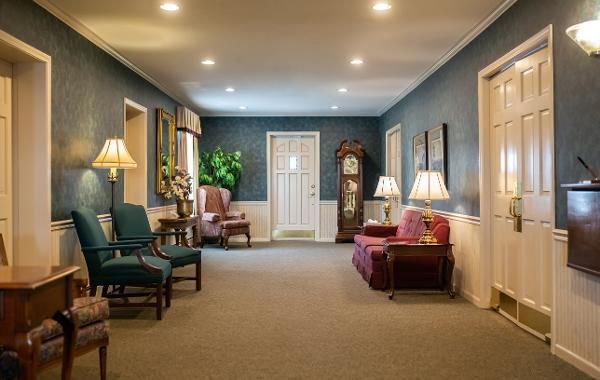 Quiet lounge with armchairs, lamps, carpeted floor, and a windowed wall in warm lighting.