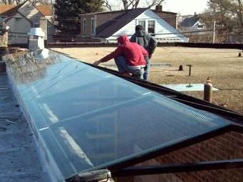 Two men are working on a glass skylight on the roof of a building.