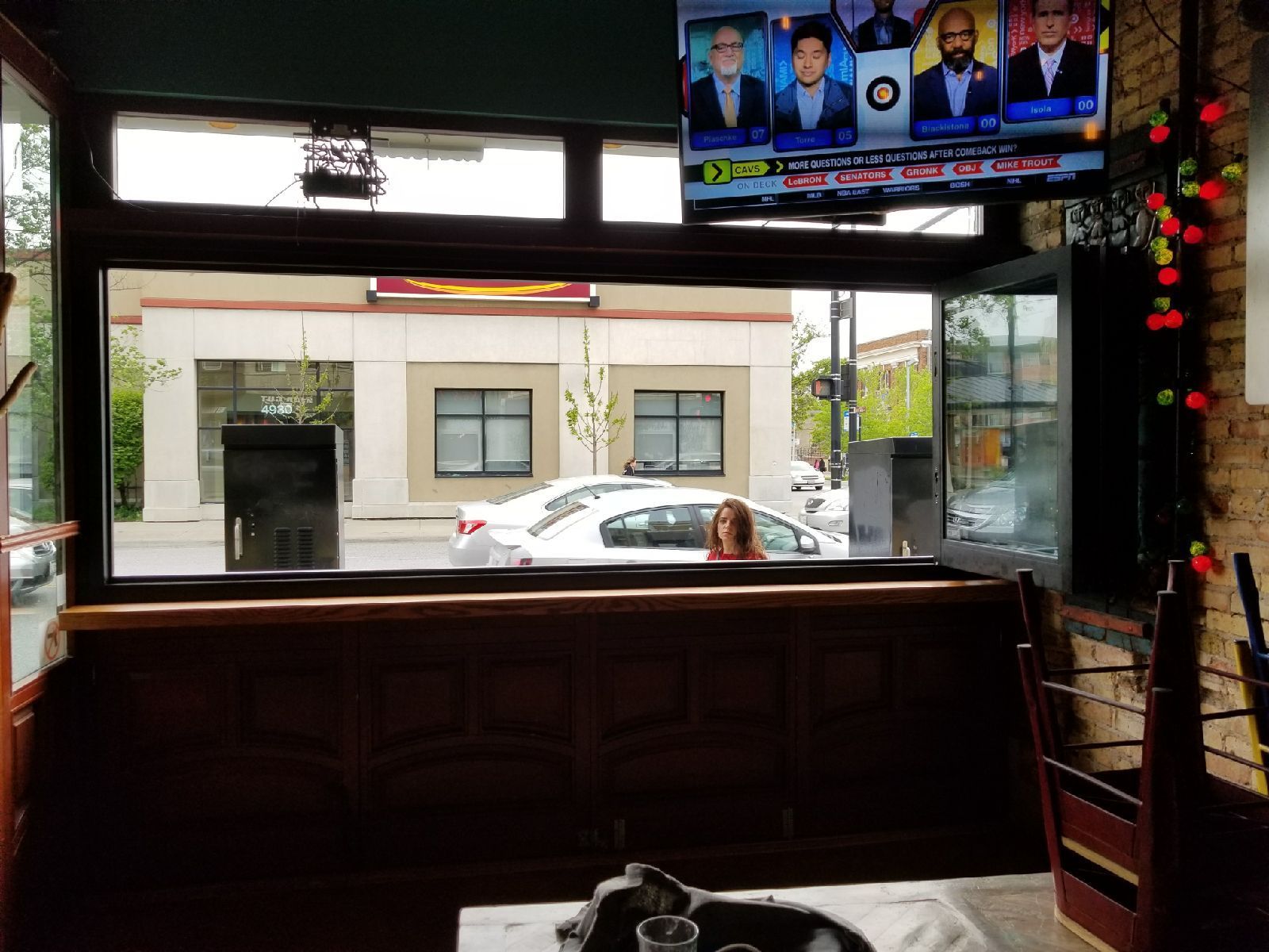 A woman is sitting at a table in a restaurant looking out a window at a street.