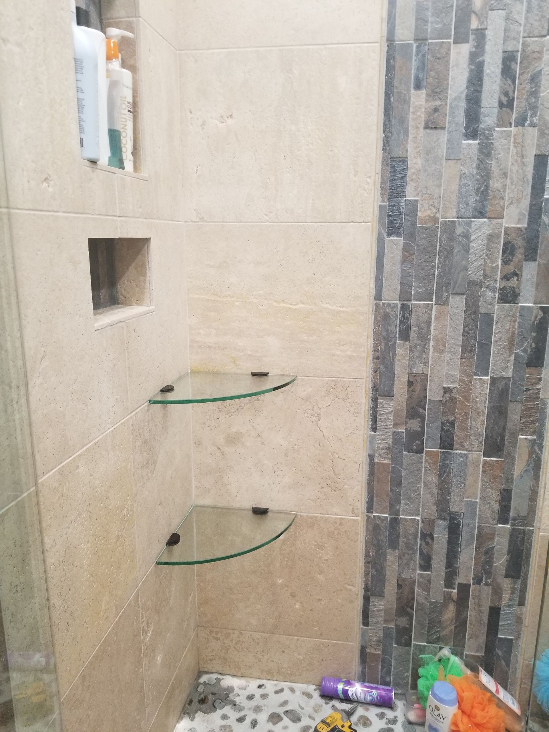 A bathroom with a shower stall and glass shelves.
