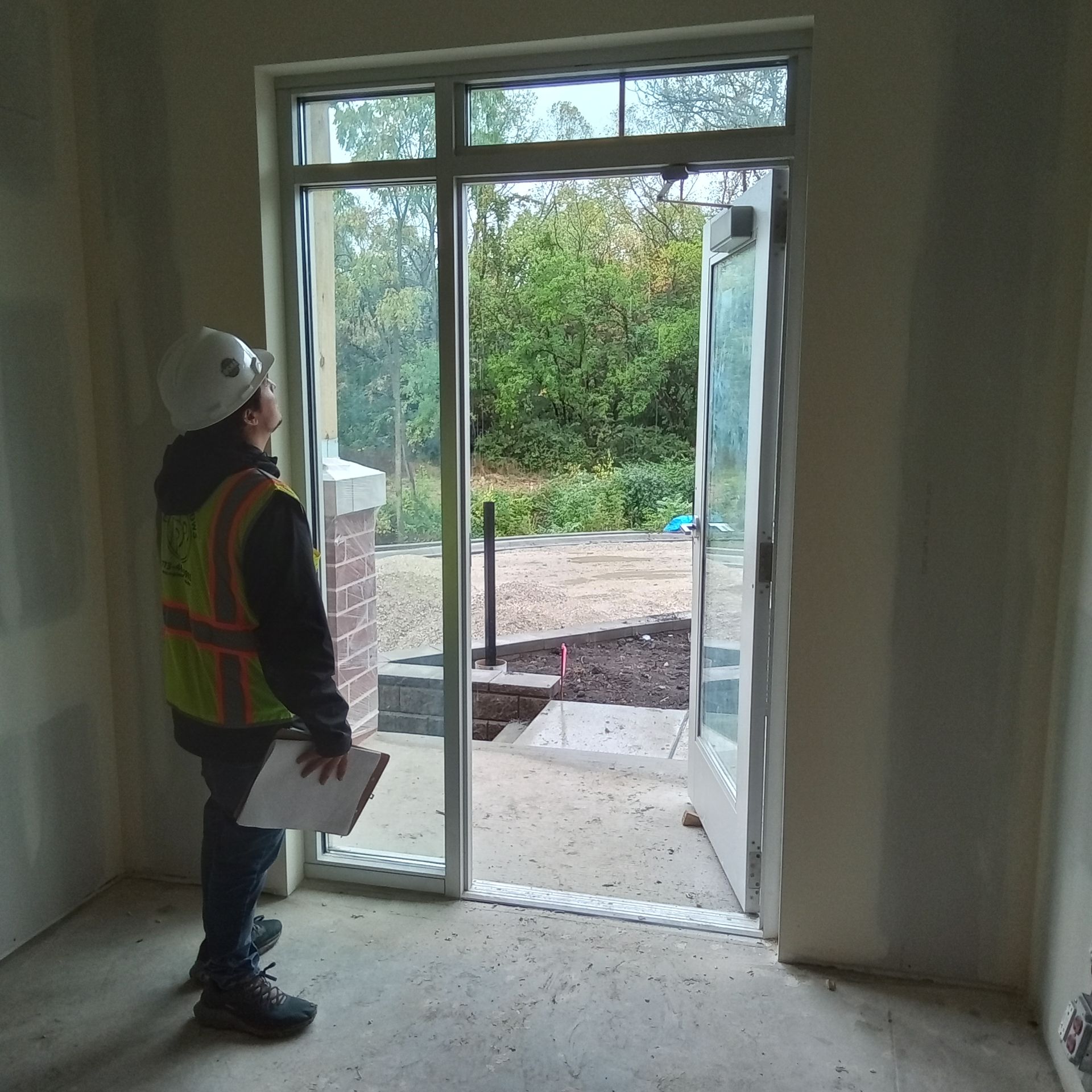 A man wearing a hard hat and safety vest is standing in front of a door