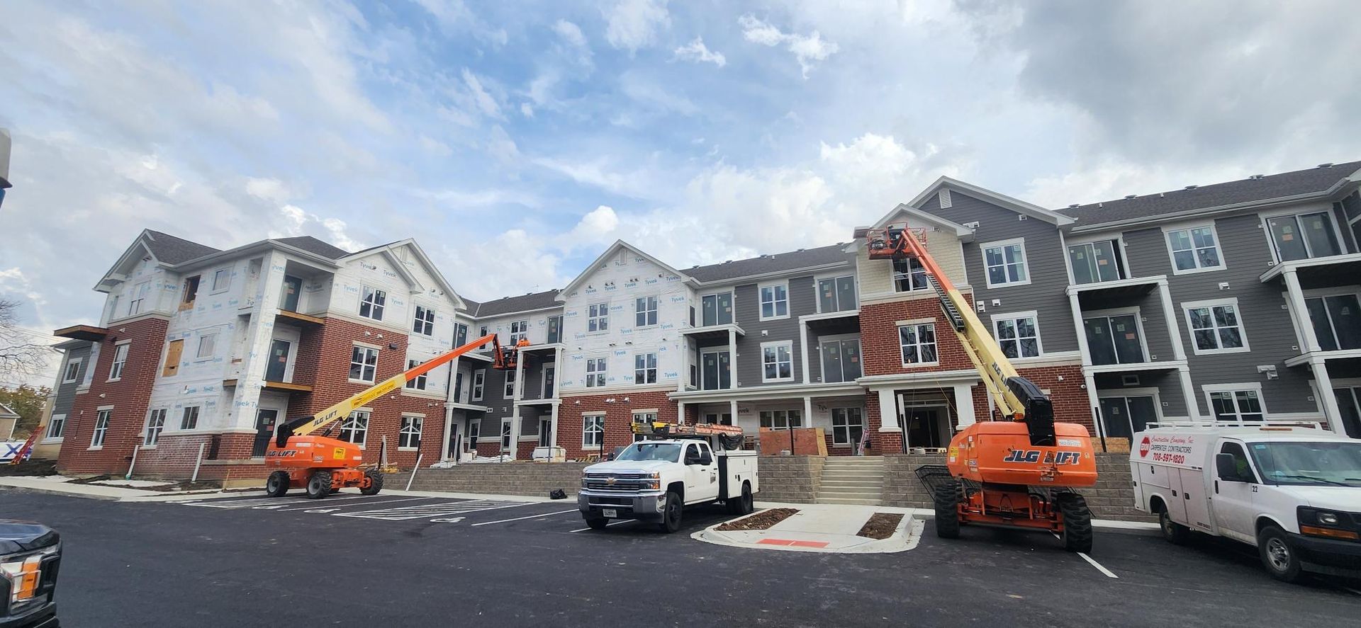 A large apartment building under construction with trucks parked in front of it.
