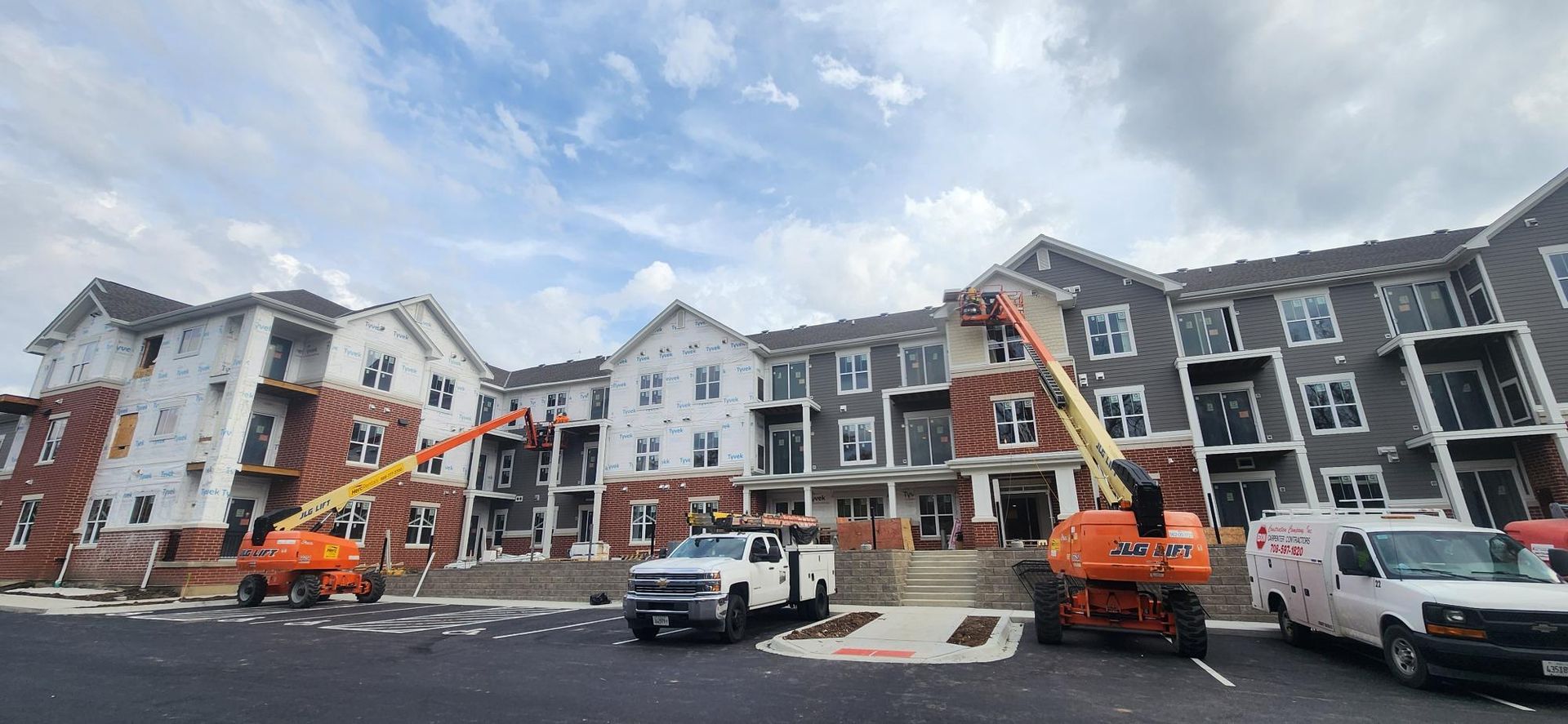 A large apartment building under construction with trucks parked in front of it.