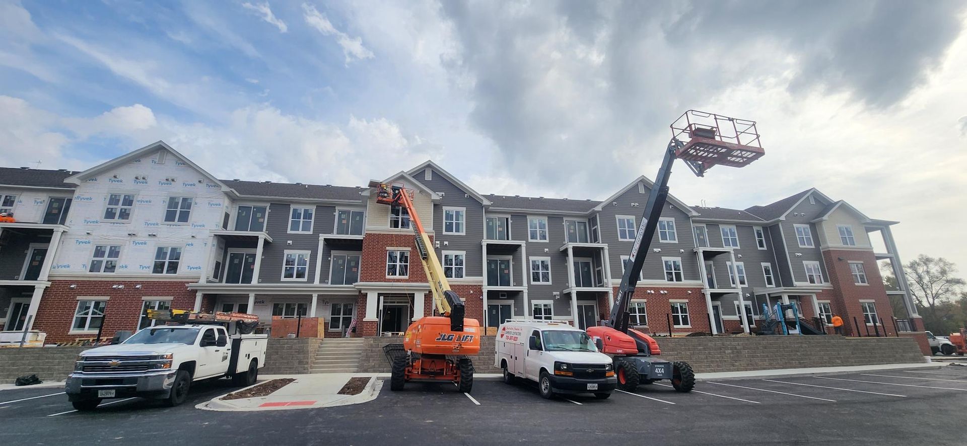A large apartment building under construction with trucks parked in front of it.